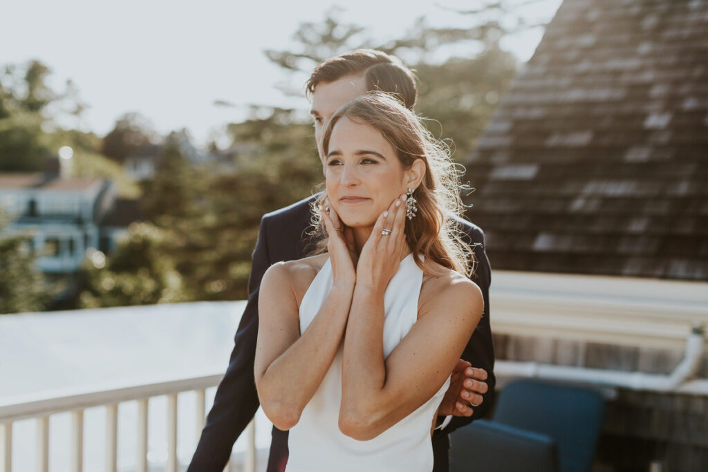 bride hold her face and smiles with groom standing behind her after Cape Cod wedding ceremony