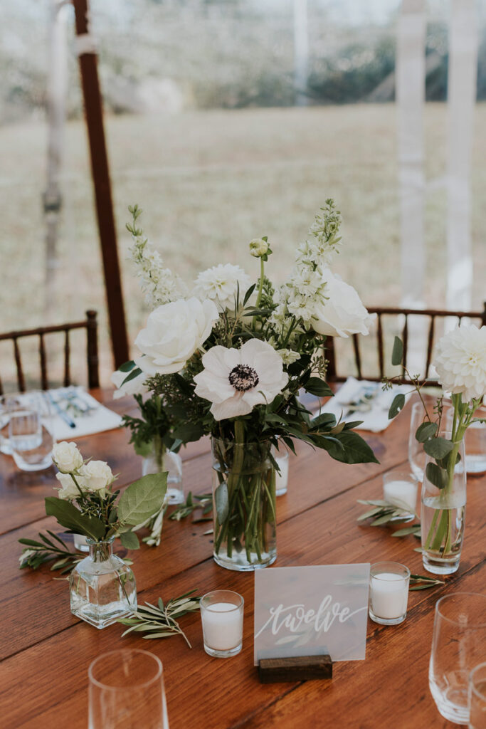 white poppies and roses in a vase on a wooden table at a wedding reception