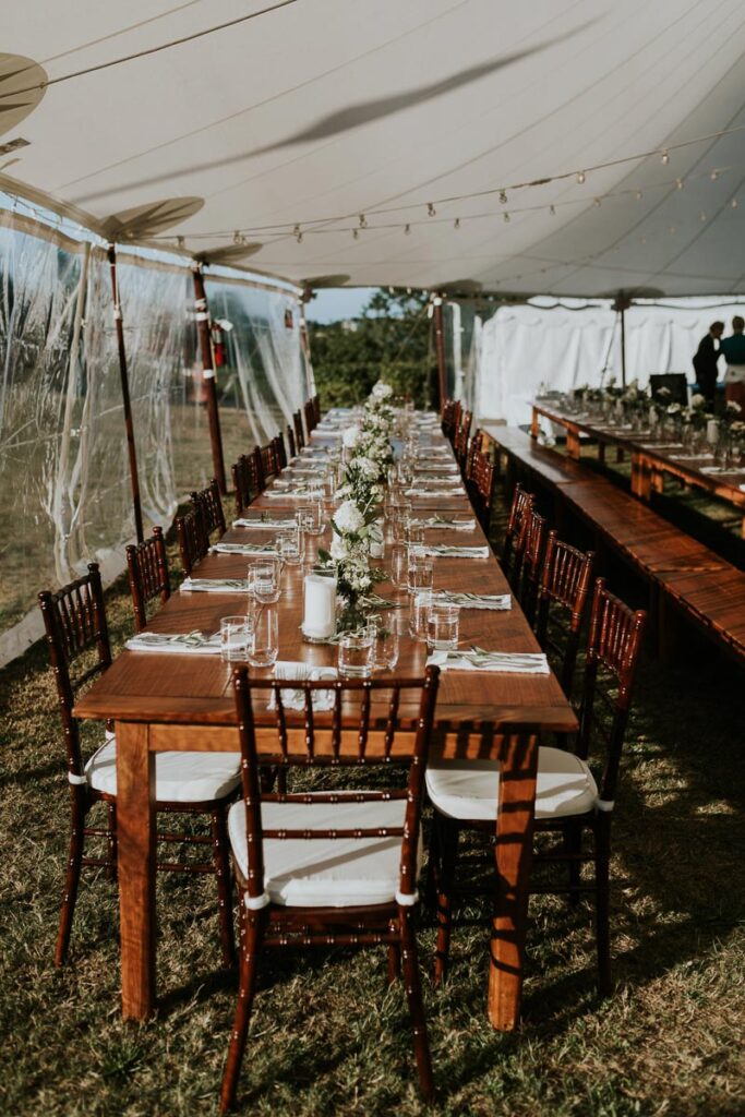 long view of a reception table adorned with a variety of white flowers in individual vases under a reception tent