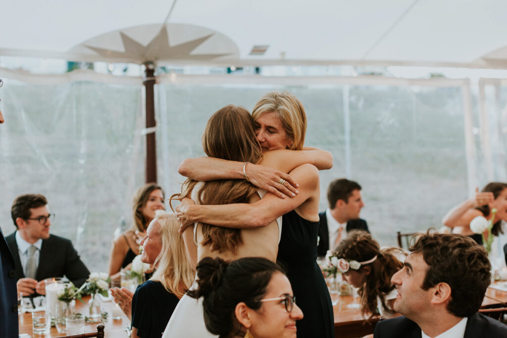 long-haired brunette bride hugs her beautiful blonde mother at a Cape Cod wedding reception