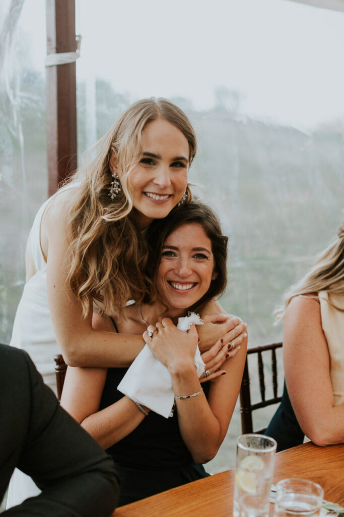 bride hugs her bridesmaid and both smile during her Cape Cod wedding reception