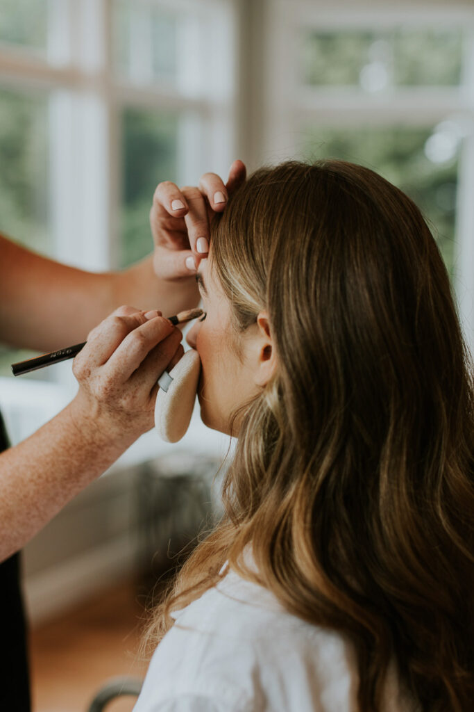 makeup artist applies eyeliner to bride on wedding day