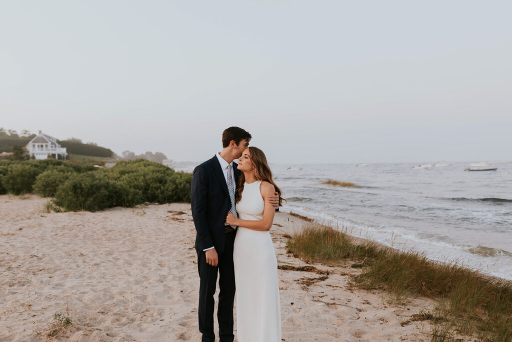 groom kisses his bride's forehead on the beach in Cape Cod