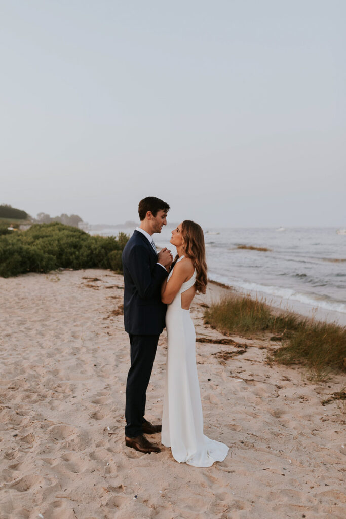 bride and groom look into each other's eyes, smiling, on the beach in Cape Cod