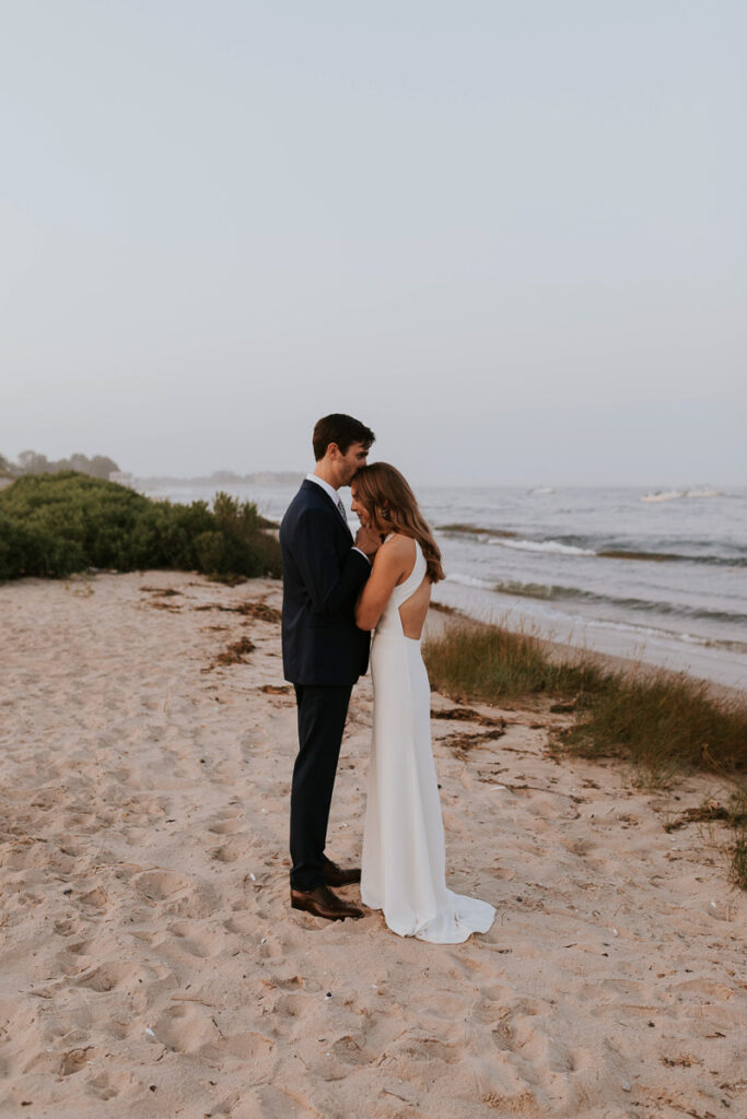 Groom kisses the top of his bride's head on the beach at Cape Cod