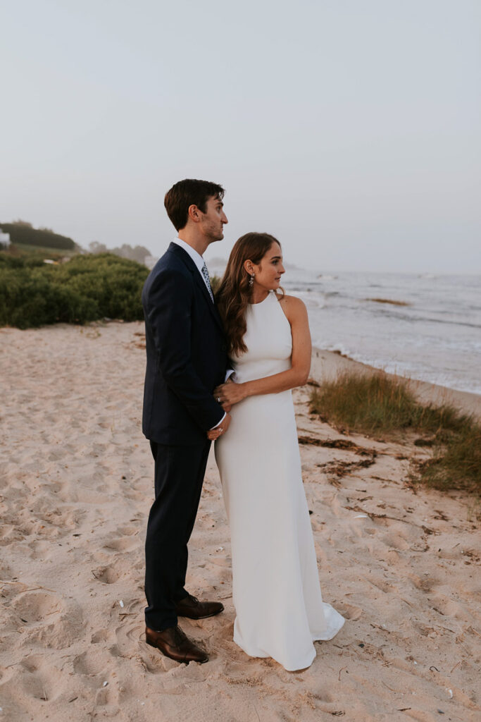 Cape Cod bride and groom stand on the beach looking out at the ocean
