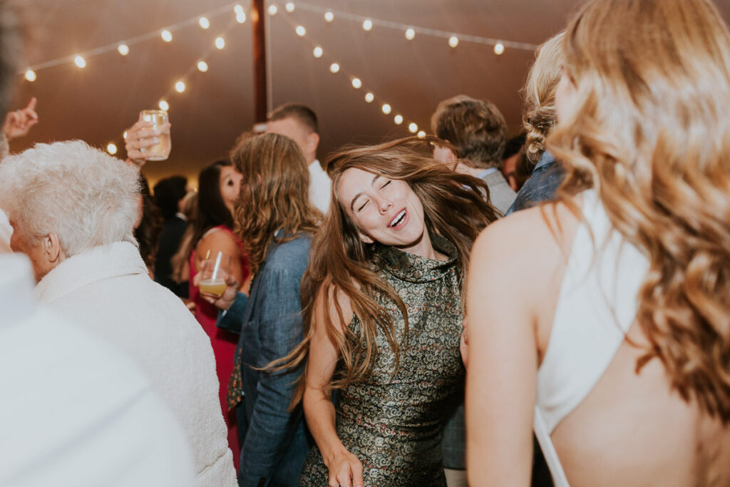 woman wearing shiny patterned dress dances and flings her hair on the dancefloor during a Cape Cod wedding reception