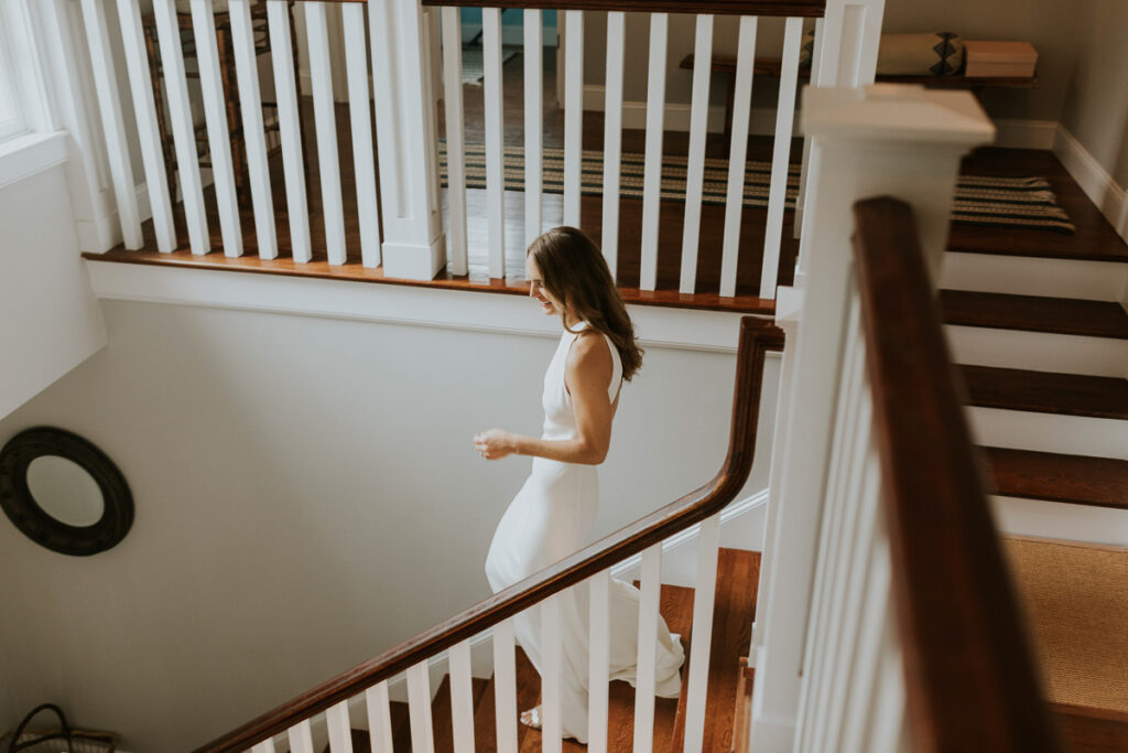 bride walks down stairs toward her bridesmaids after putting final touches on her outfit