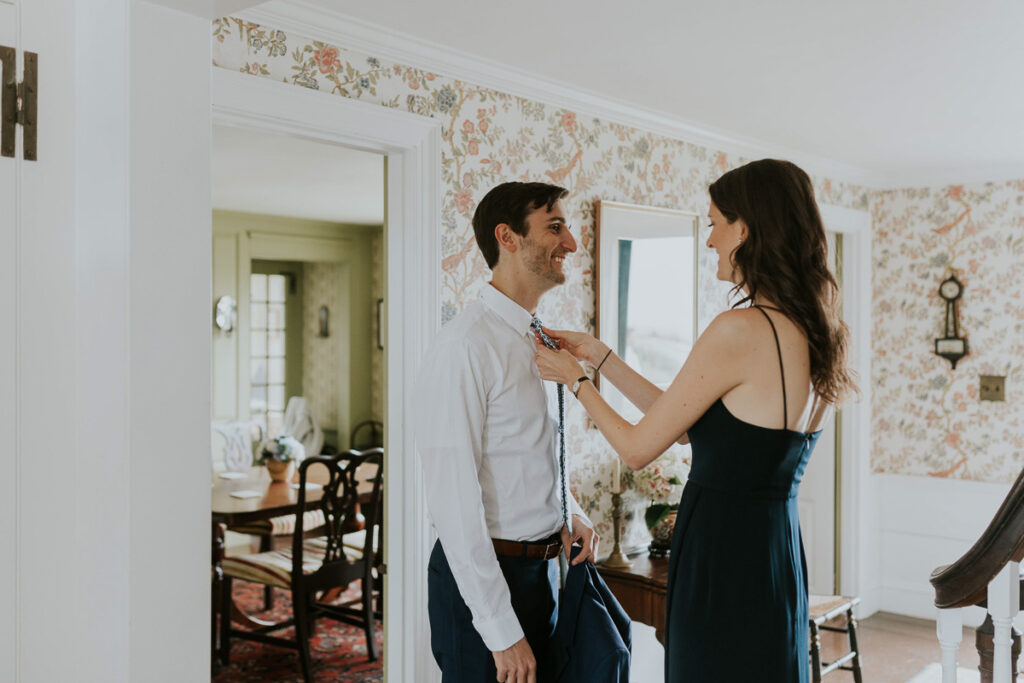Best Woman and groom smile and laugh while she assists in tying his tie