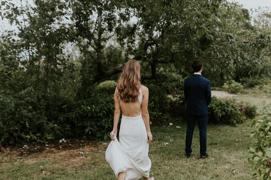 bride walks toward groom, while he faces away from her waiting to see her in first look