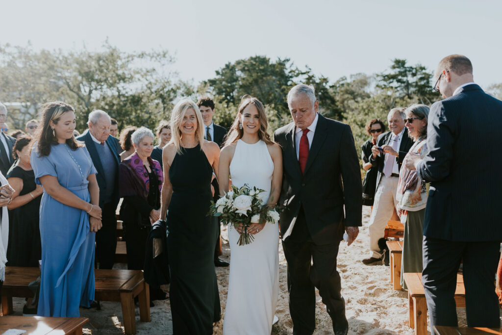 Bride is walked down the aisle by her parents in Cape Cod beach wedding