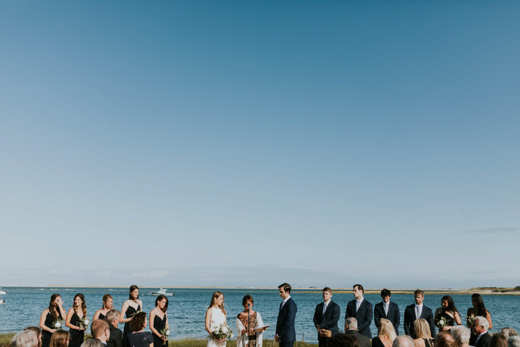 Far off image of entire bridal party and ocean during beachfront wedding in Cape Cod