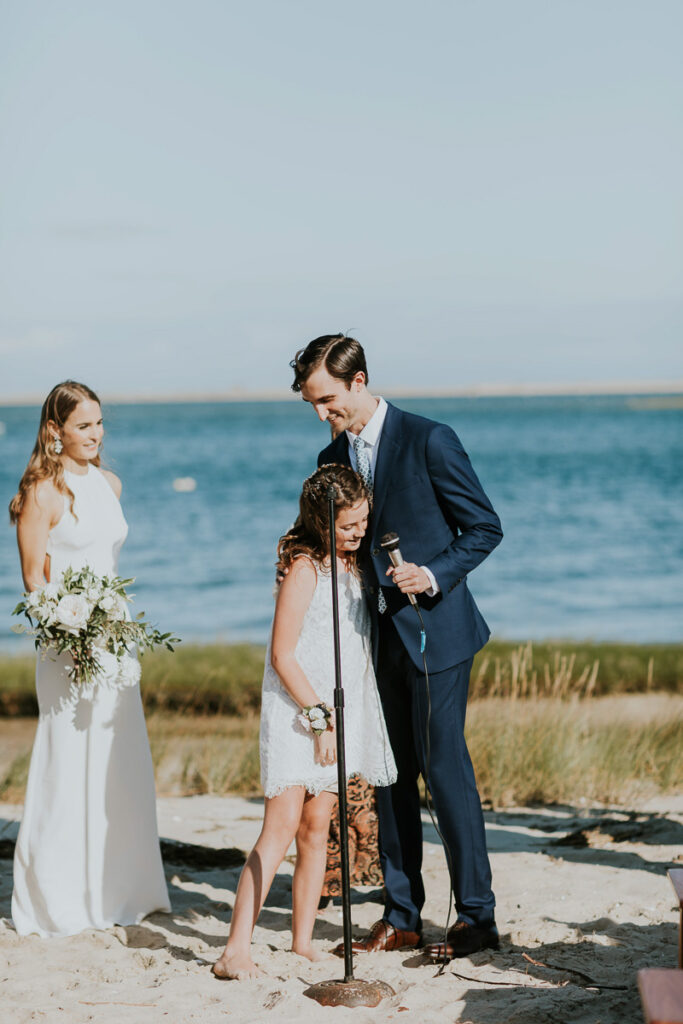 Groom hugs flower girl during marriage ceremony on Cape Cod